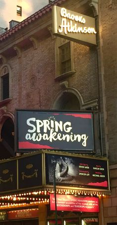 a theater sign is lit up in front of an old brick building that has the words spring awakening on it