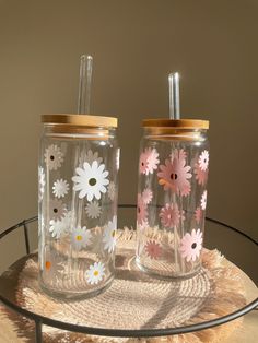 two glass jars with flowers painted on them are sitting on a table next to each other