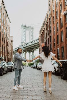 a man and woman holding hands while walking down the street in front of tall buildings