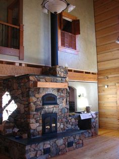 a large stone fireplace in the middle of a room with wooden floors and walls, surrounded by wood paneling