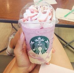 a person holding up a starbucks drink with pink liquid and whipped cream on the top