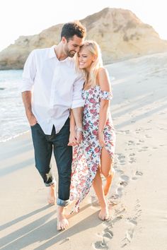 a man and woman walking on the beach holding hands with footprints in the sand behind them