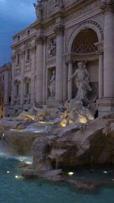 a fountain in front of a large building with statues on it's sides at night