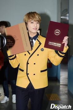 a man in a yellow jacket holding two boxes on his shoulders and wearing a suit