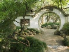 an arch in the middle of a garden with rocks and trees around it, surrounded by greenery