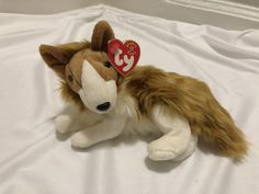 a brown and white stuffed animal laying on top of a white bed sheet with a red heart