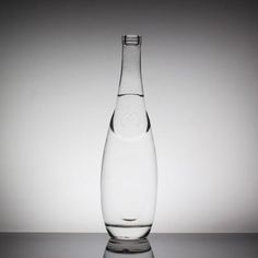 a glass bottle filled with water sitting on top of a reflective surface, in front of a gray background