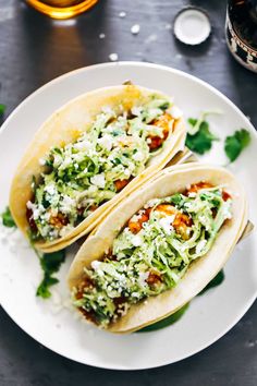 two tacos on a white plate topped with shredded lettuce