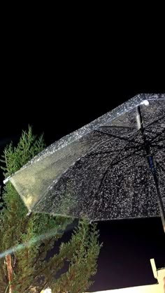 an open umbrella with water droplets on it and trees in the foreground at night