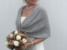 a woman wearing a gray shawl holding a bouquet of white and pink flowers in her hands