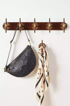 a purse hanging on a wall next to a scarf rack with two scarves and a handbag