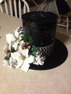 a black hat sitting on top of a table next to white and green flowers in front of it