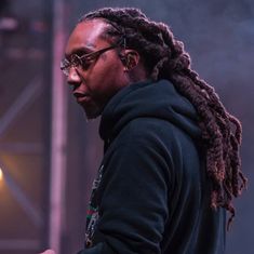 a man with dreadlocks and glasses holding a cell phone in his right hand