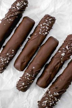 four chocolate covered donuts are lined up on wax paper with white sprinkles