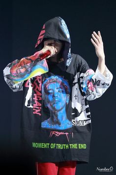 a young man wearing a black hoodie and red sweatpants is holding his hands up to his mouth