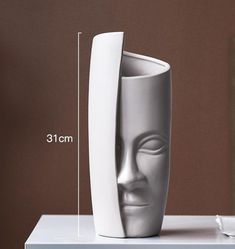 a white vase sitting on top of a table next to a cup with a face in it