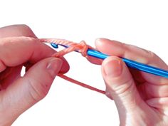 two hands are holding an orange and blue crochet hook with one hand while the other is knitting