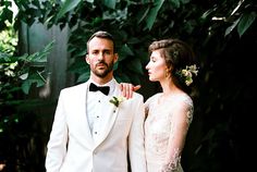 a man and woman standing next to each other in front of some trees with greenery