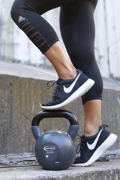 a woman in black and white running clothes lifting a kettle with her feet on the ground