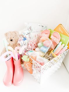 a basket filled with lots of items and a teddy bear sitting next to some rubber boots