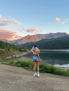 a woman standing on top of a dirt road next to a lake