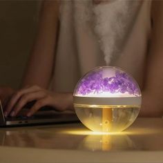 a person sitting at a table with a laptop in front of them and a bubble lamp on top of it