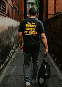 a man walking down the street with a bag in his hand and wearing a t - shirt that says, be by every word of god