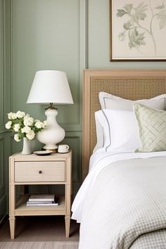 a bedroom with green walls, white bedding and flowers on the night stand in front of the bed