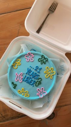 a cake in a plastic container with a fork on the table next to it that says happy little's