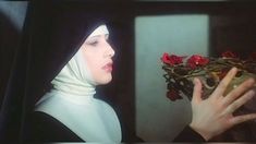 a nun holding flowers in her hand and looking at the viewer's face with both hands