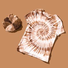 a brown and white tie - dye shirt next to a hat on a tan background