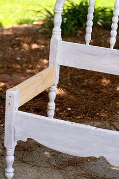 a white wooden bed frame sitting on top of a dirt ground next to a tree