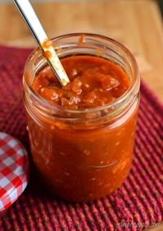 a jar filled with sauce sitting on top of a red and white checkered table cloth