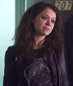 a woman with long hair wearing a leather jacket and looking off into the distance while standing in front of a door