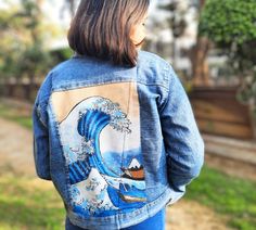 a woman wearing a denim jacket with an image of a wave painted on the back