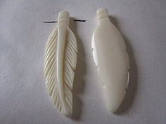 two pieces of carved ivory are sitting on a white tablecloth, one is shaped like a bird's wing and the other has a black string attached to it