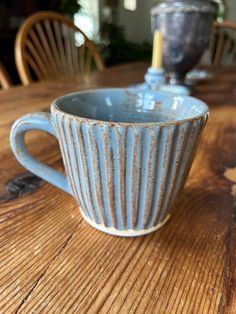 a blue coffee cup sitting on top of a wooden table next to a candle holder