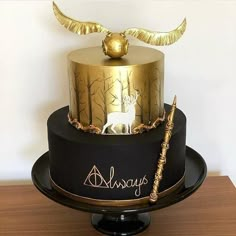 a black and gold cake with an angel decoration on top is sitting on a wooden table