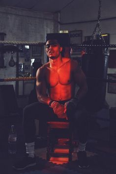 a shirtless man sitting on a chair in a boxing ring with his hands behind his back