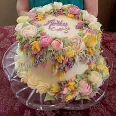 a birthday cake decorated with flowers and the words happy birthday written on it is sitting on a glass platter