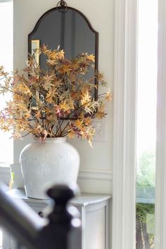 a white vase filled with flowers sitting on top of a table next to a mirror