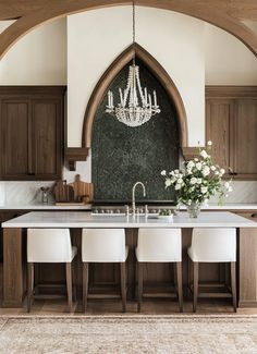 a kitchen with an arched window and chandelier hanging from the ceiling, surrounded by white chairs