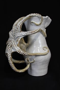 an octopus mask is on display in front of a white vase with gold accents and pearls