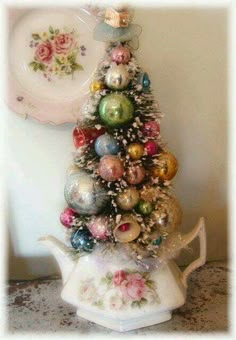 a small christmas tree with ornaments on it in front of a white plate and wall