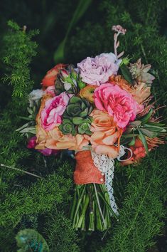 a bridal bouquet with pink and orange flowers on green grass in the evening light