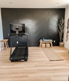 there is a treadmill in the middle of this room with black walls and wood flooring