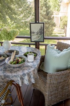 the table is set on the porch with plates and bowls of food in front of it