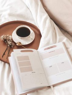 an open book on a bed next to a cup of coffee and a plant with dried flowers