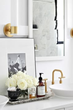 a bathroom vanity with flowers, soap and lotion in front of a framed photograph