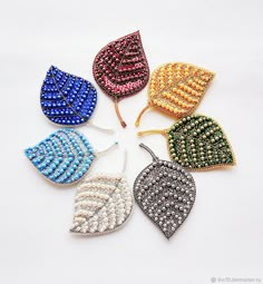 six different colors of beaded leaves are arranged in a circle on a white surface